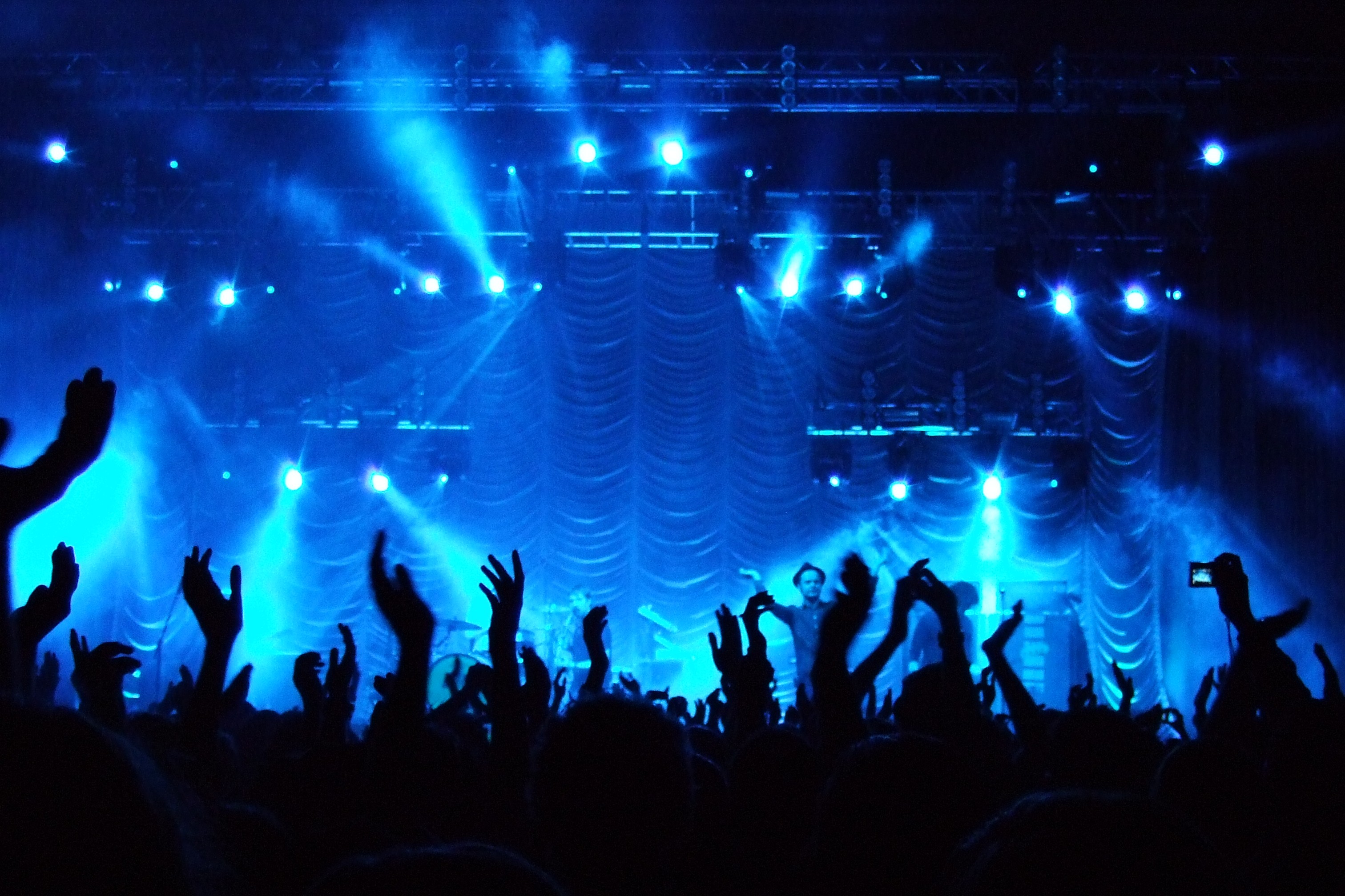 Photo of a concert where the lighting is blue and the singer is pointing the microphone to the crowd