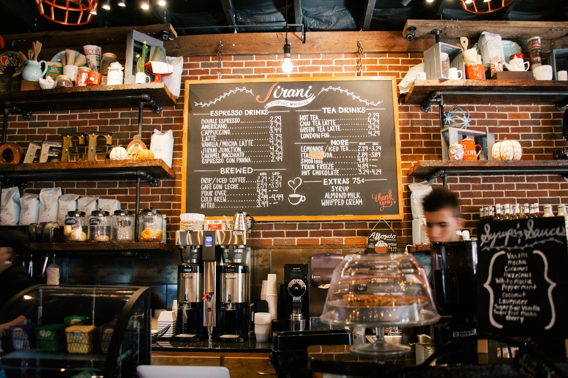A barista behind the counter at a coffee shop, menu and spice jars in full display