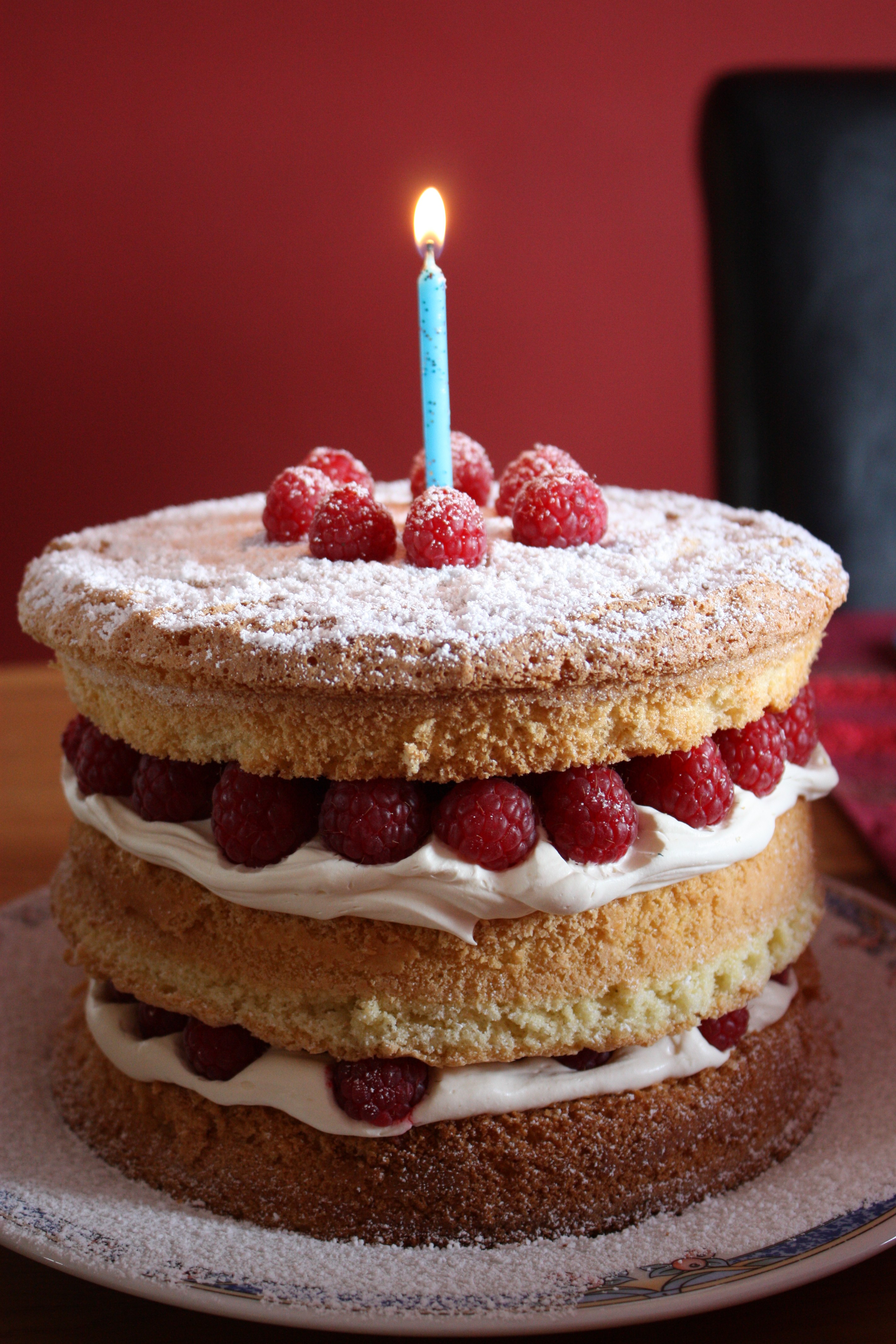 A birthday cake covered in raspberries, whipped cream, and powdered sugar.