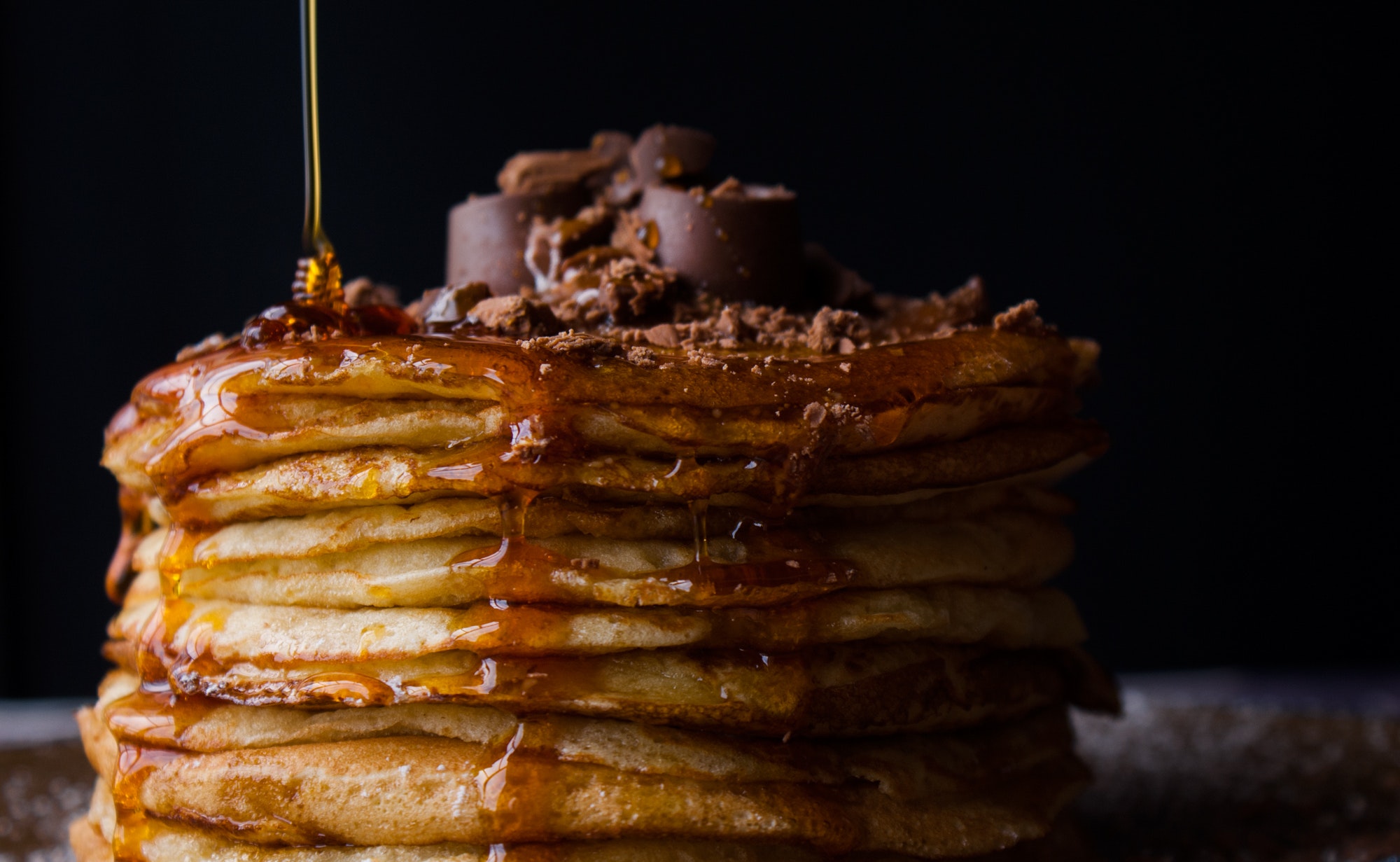A stack of pancakes covered in cocoa nibs, maple syrup, and honey. Delicious!