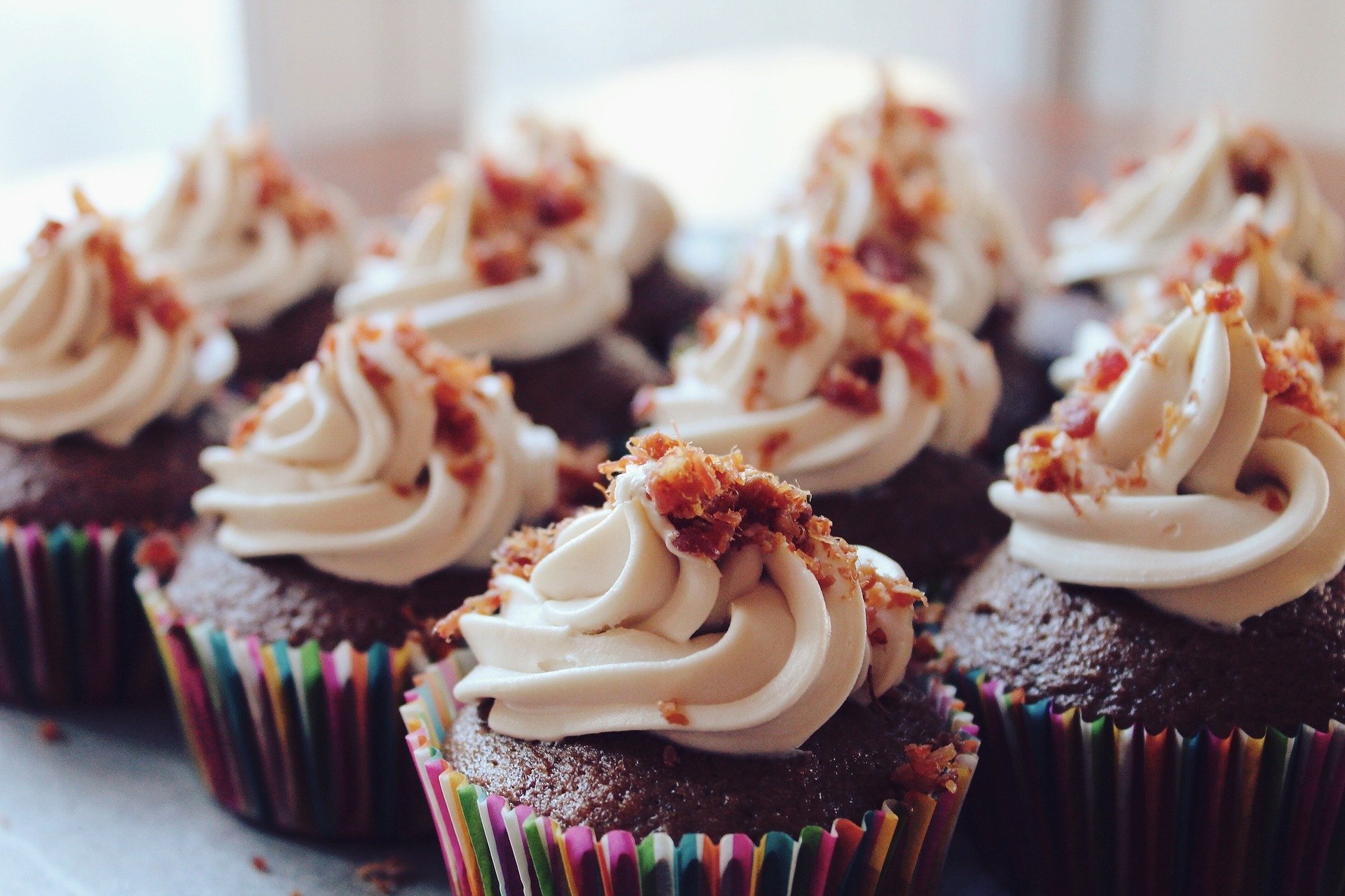An array of chocolate cupcakes in rainbow wrappers with a maple icing and bacon crumbles. Yum!