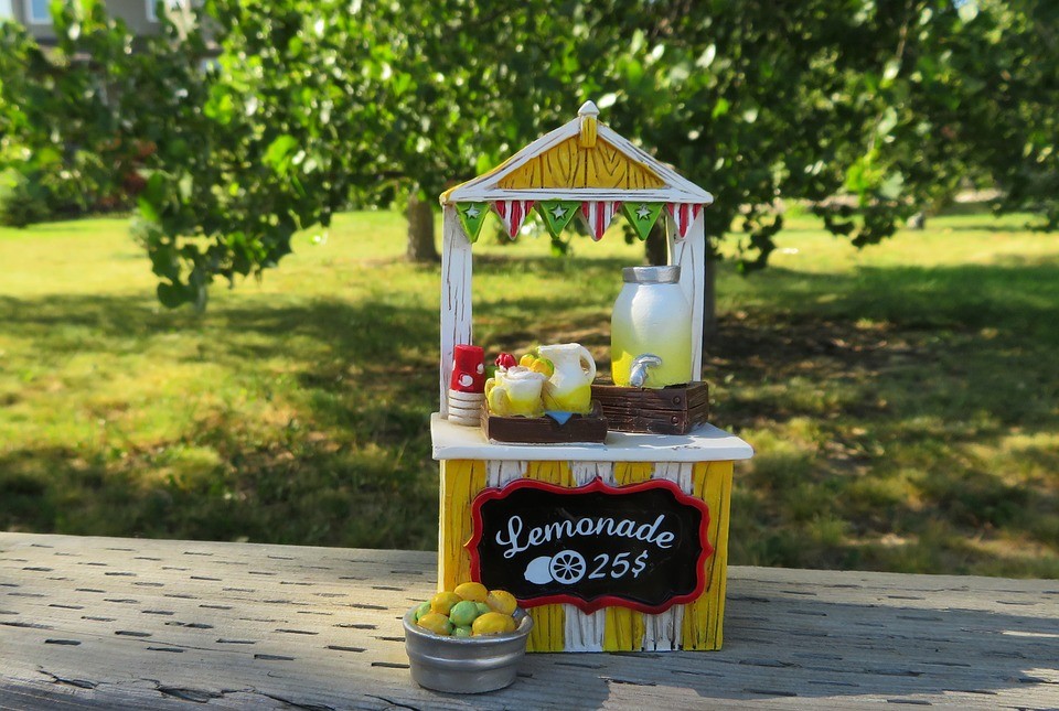 A cute lemonade stand painted yellow and white, with a sign on the front that says "Lemonade 25 cents"