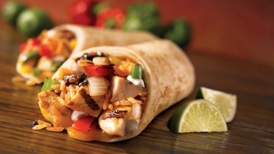 A picture of a tasty looking chicken burrito, with two lime slices sitting next to it.