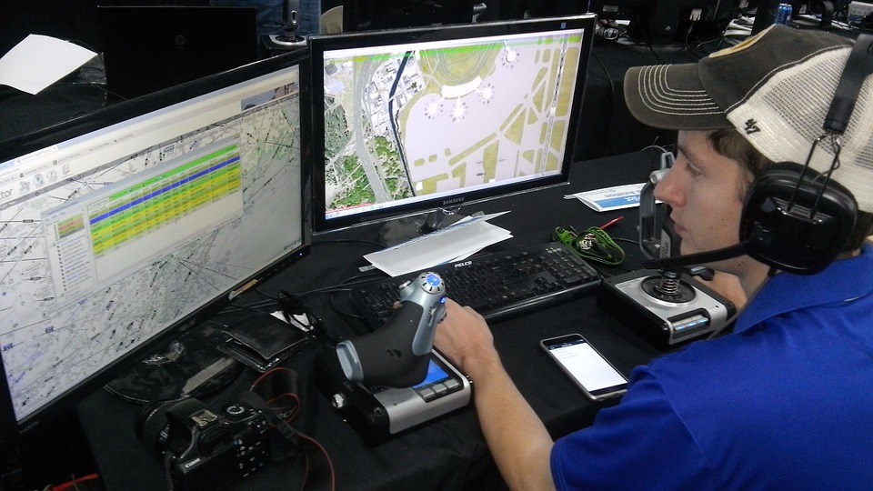 Picture of an air traffic controller sitting at a desk with 2 computer monitors in front of him.  He is wearing a headset to communicate with the active planes.
