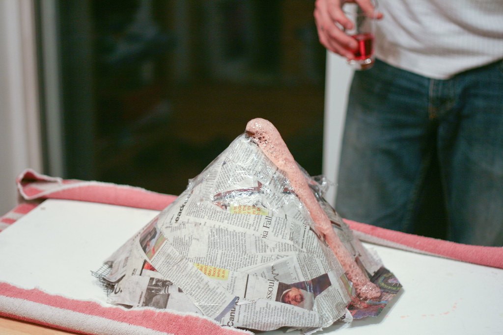 Image description: a homemade volcano made from paper maché. There is "lava" spilling out from vinegar, baking soda, and red food dye.