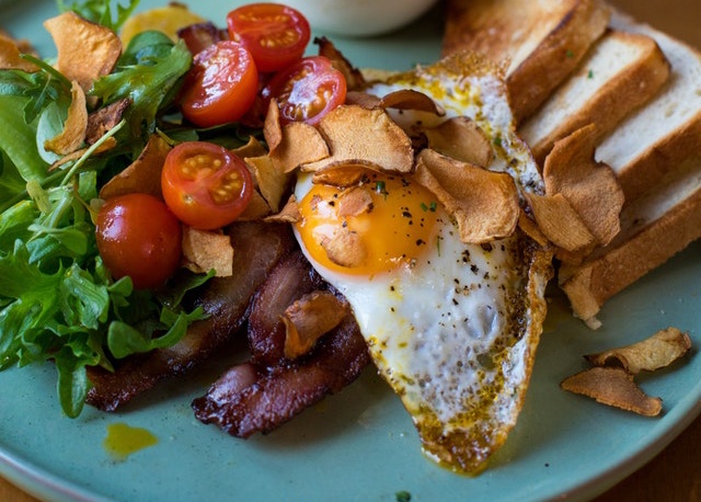 Eggs, bacon, chips, toast, arugula, and tomatoes.