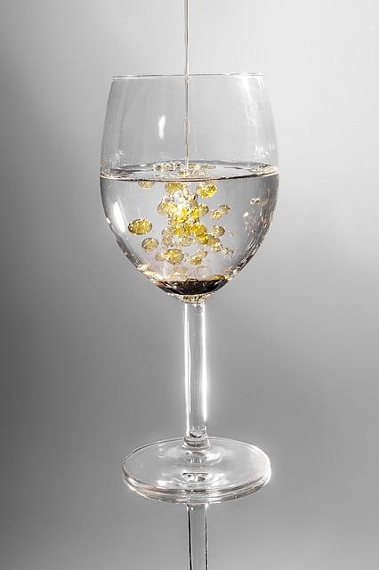 Oil is being poured into a glass. The oil sticks together to form bubbles that do not dissolve in the water.