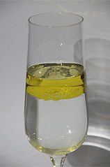 A glass filled with oil and water. The oil rises to the top of the glass.