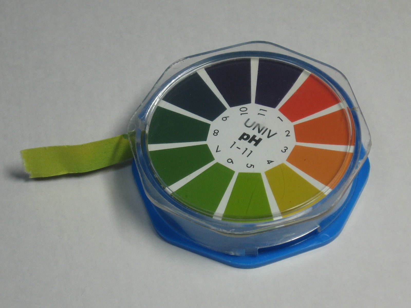 Photograph of a piece of indicator paper and the corresponding scale identifying each pH level based on the color of the paper when placed in that solution.