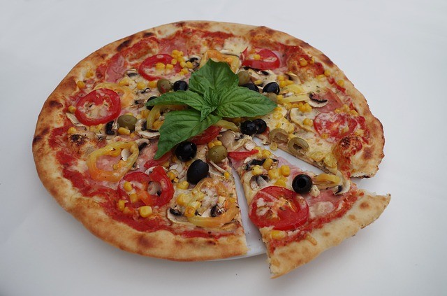 A pizza with red and yellow peppers, corn, basil, and olives