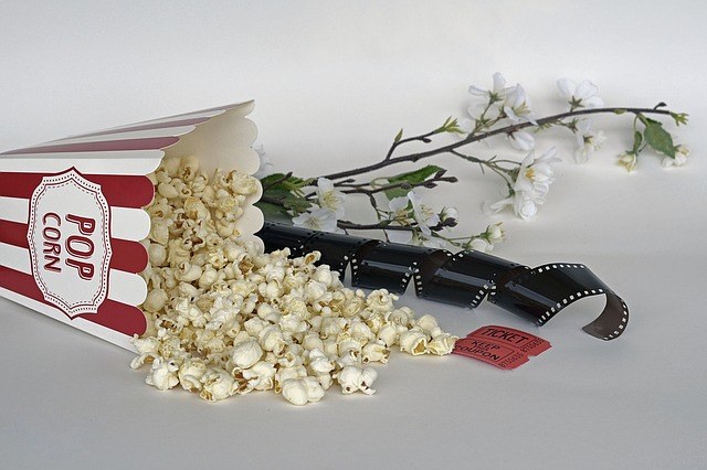 A bag of popcorn, tickets, movie film, and a flower