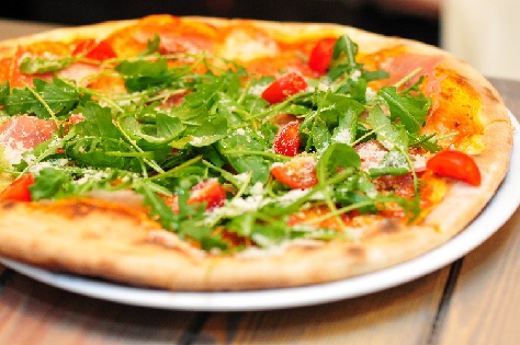 A pizza with spinach, tomatoes, and a sprinkling of cheese.