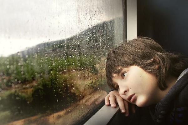 Kid staring out a rainy window.