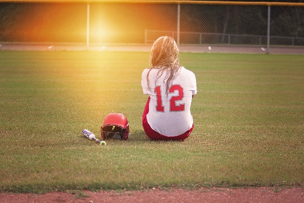 A picture of a girl sitting on a baseball field.