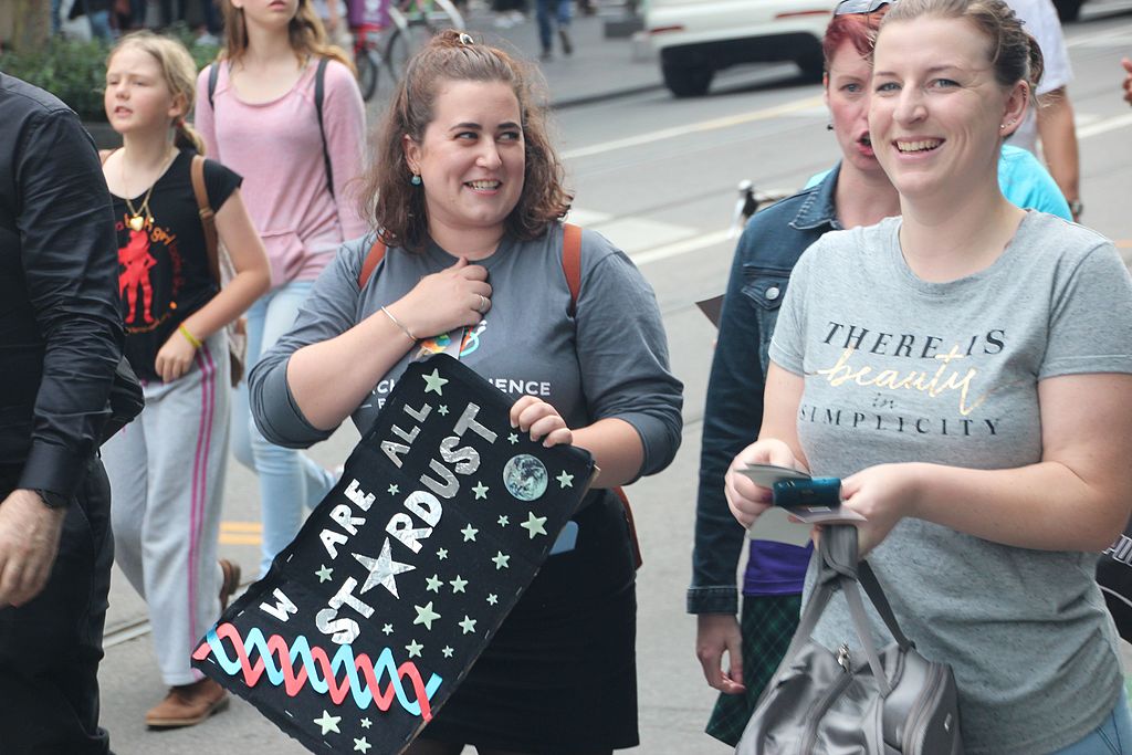 Photograph of individuals at the March for Science in 2017, with a woman at the front holding a sign that says "We are all stardust".
