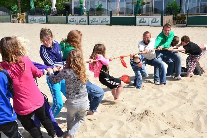 Photograph of children and adults playing Tug of War in the sand.