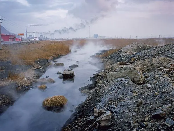 The image shows s polluted stream with a factory in the distance.