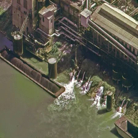 The image shows a factory releasing wastewater into a river.